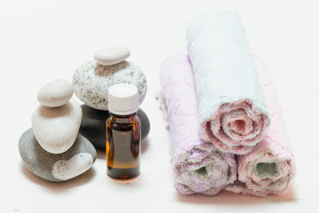 Aromatherapy oil, pebbles and rolled up towels on white background.
