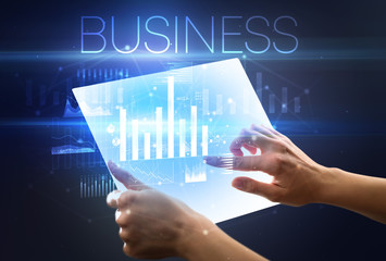 Hand holding futuristic tablet with BUSINESS inscription above, modern business concept