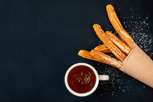 Churros with sugar powder with chocolate sauce dip  on dark background, top view. Copy space