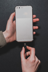 close-up of female hands that plug a smartphone into charging on a black background