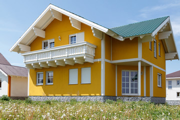 New yellow house with white windows and a large wooden balcony built in the village.