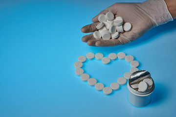 The doctor holds white pills in hand on a blue background. White pills and a bottle lie in the form of a heart. medical template