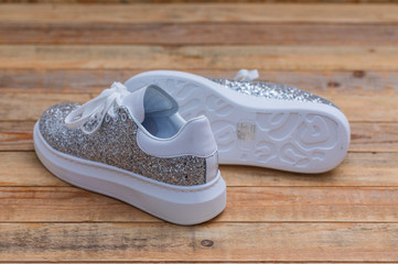 Glittery sneakers on wood background, close-up