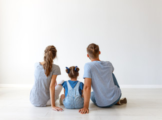 happy family mother, father and child daughter   backs on blank grey wall