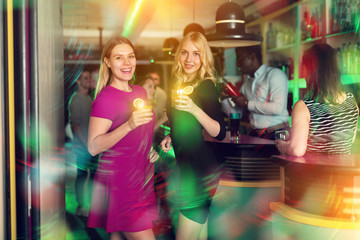 Two young women with cocktails having fun on party at nightclub