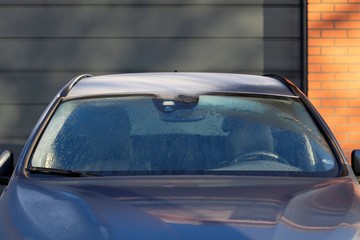 A frontal portrait of the frozen windshield of a car which is already almost melted so the driver...