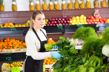 Young female seller in gloves working with greens and letuce