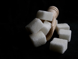 sugar cubes and wood spoon over black background