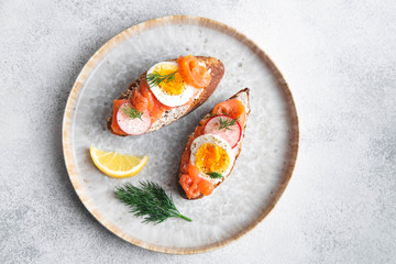 Italian appetizer bruschetta with red fish, boiled egg, cream cheese, radish and dill on a plate on a white background, close up top view horizontal
