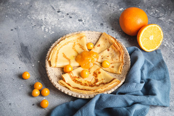 Russian cisine, pancakes with orange jam and berries, on a plate on a grey background. Maslenitsa week festival. Close-up horizontal.