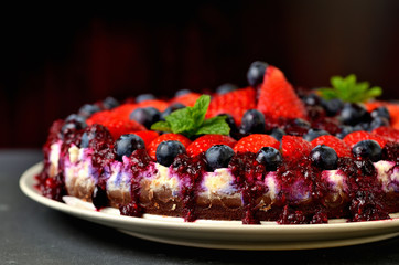 Tart with fresh strawberries, blueberries and cherry jam. Dark background. Low depth of field