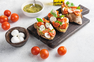 Italian snack bruschetta with tomatoes, mozzarella and basil on a dark wooden board on a white background, close up horizontal