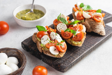 Italian snack bruschetta with tomatoes, mozzarella and basil on a dark wooden board on a white background, close up horizontal