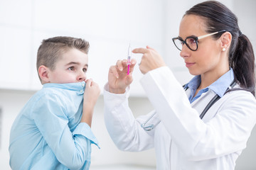 The boy is afraid of injections before preventing vaccination. Young doctor preparing a vaccine for a boy in an ambulance