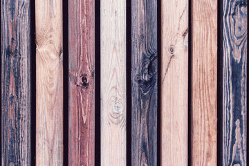 Rustic wooden fence made from treated differently colored boards. Vertical background wall made of vintage pine wood in vintage style.