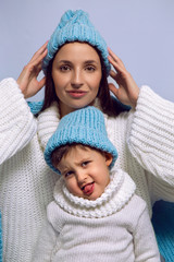 mother and son in white sweaters and blue hats stand on a blue background