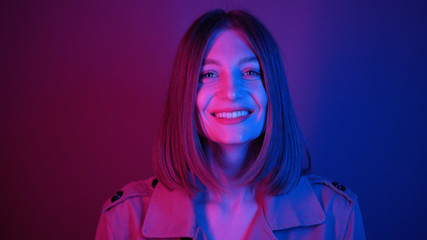 Lovely young woman with straight hair looking at camera. Amazing purple neon lightning. Shooting of attractive girl with blue eyes. Look. Beautiful Caucasian model. Colourful.