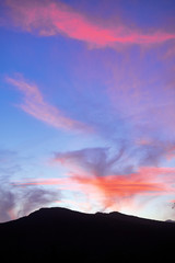 Blue sky during sunset and with clouds of different sizes and shapes, with intense yellow and red colors. Mountain in the lower part of the image.
