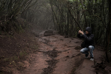 Man traveler in blue raincoat enjoying hiking in the beautiful scary mystic rainforest trees in Anaga national park on Tenerife island, Spain. Rain, fog, silence in old forest