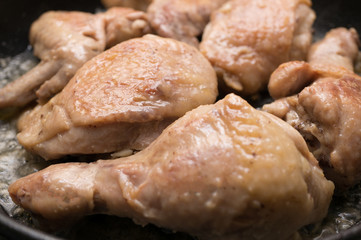 Chicken pieces are fried in a pan. Close-up, soft focus, shallow depth of field.