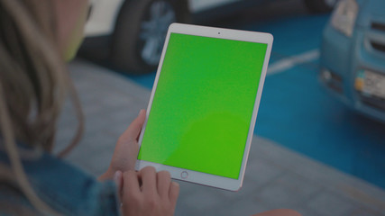 Lviv, Ukraine - May 19, 2018: Close-up of young woman using mock-up vertical tablet computer with green screen swiping pages while staying outdoors in the street. Modern lifestyle.