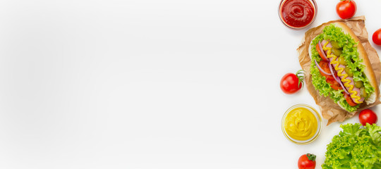 Hot dog with pickles, tomatoes and lettuce on a white background. Fast food. Calorie food. View from above. Space for copy. Food banner.