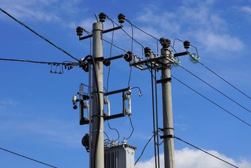 two gray concrete pillars with electric wires on a background of blue sky and clouds on a sunny day