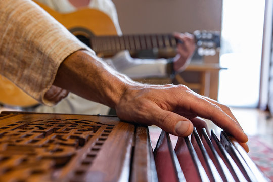 Closeup Of Senior Hands Playing Indian Classical Sacred Kirtan Music For Silence And Peace Using Harmonium With Woman Playing Classical Guitar