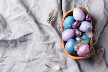Easter. Festive bright eggs in a wooden bowl on a background of gray cotton fabric. Top view. Space...