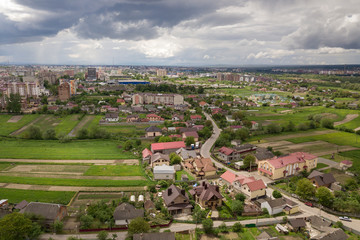 Aerial view of town or village with rows of buildings and curvy streets between green fields in summer. Countryside landscape from above.