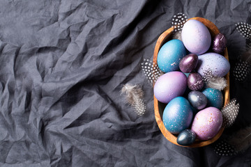 Easter. Festive bright eggs in a wooden bowl on a background of gray cotton fabric. Top view. Space for text.
