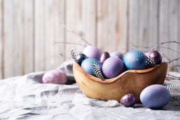 Easter. Festive bright eggs in a wooden bowl on a background of gray cotton fabric and wood wall. Space for text.