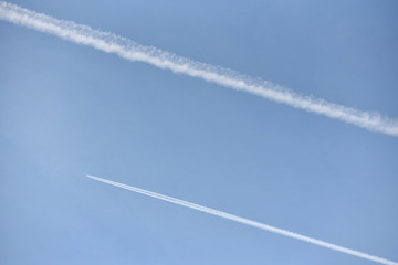 A passenger plane flies high in the sky and leaves a white trail against the blue sky. Text space