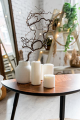 white candles on wooden coffee table in cozy living room interior.Stylish scandinavian living room.Candle and plant in vase on small wooden table in front of scandinavian designed sofa. boho home