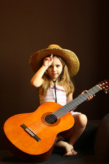 Portrait of a caucasian toddler girl wearing a straw hat and holding the guitar