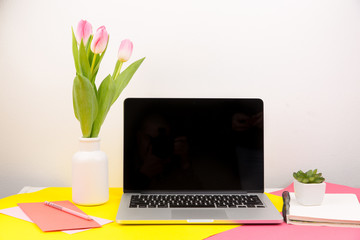 Office desktop.Laptop with tulips ,coffee and notebook on wooden table