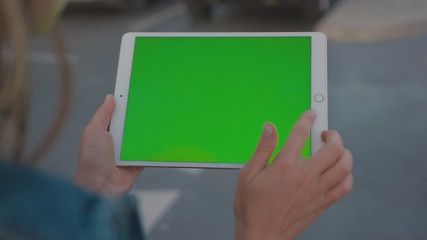 Lviv, Ukraine - May 19, 2018: Close-up of girl holding vertical tablet digital computer with mock-up green display in busy city road during night time. Urban lifestyle.