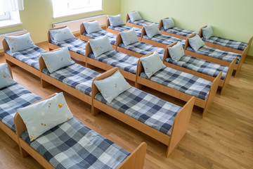 Many small beds with fresh linen in daycare preschool empty bedroom interior for comfortable afternoon nap of the kids.