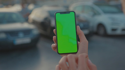 Lviv, Ukraine - May 19, 2018: Close-up of young urban girl showing vertical smartphone with greenscreen chrome key technology on parking lot outside. City life and modern gadgets. © koshkin_stock