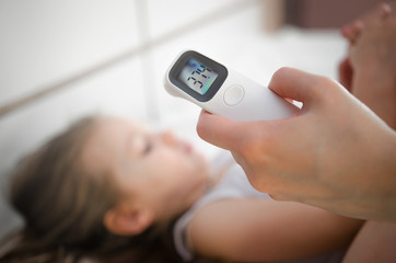 Mother takes temperature for her child with infrared thermometer at home. Mother hand holding...