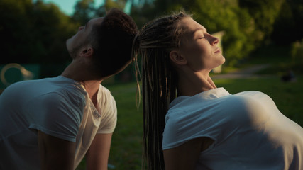 Relaxed healthy young caucasian couple meditating in bliss sitting back to back on mat practising yoga at sunset outdoors.