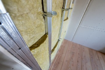 Wall of a room under renovation with mineral rock wool insulation and metal frame prepared for drywall plates.