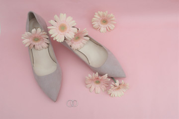 wedding concept. gerbera flowers, rings, beige shoes on a pink background.