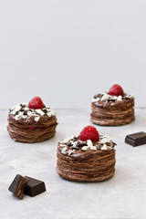 Petit fours or mini chocolate crepe cakes with strawberry on gray background