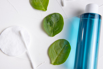 blue micellar water, green spinach leaves, cotton pads and sticks on a concrete background. with place for an inscription.
