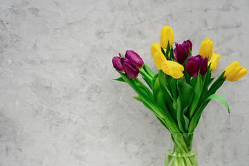 Bouquet of purple and yellow spring tulip flowers in a glass vase on a light background. Copy space. Mothers Day. International Women's Day.