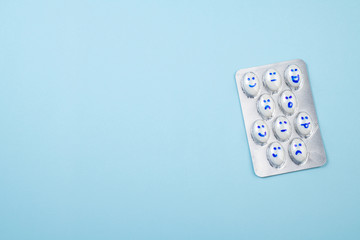 Pills and funny faces in blister on blue background. Health care, daily pills, antidepressants, medicine concept