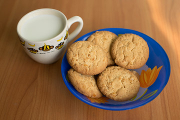 White cup with milk and cookies on wooden background. Homemade oat cookies - a sweet dessert.