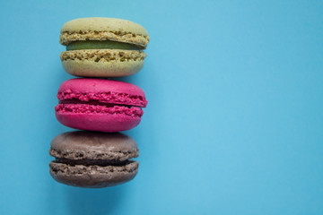Fototapeta na wymiar Three macaroons: pistachio, raspberry and chocolate on a blue background with copy space. Food photo.