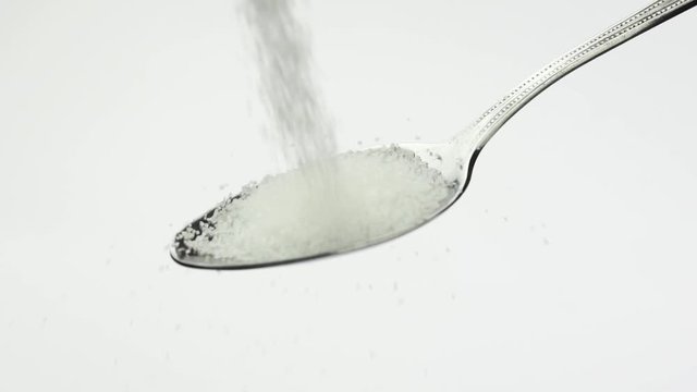 White granulated sugar fall teaspoon on a white background in slow motion